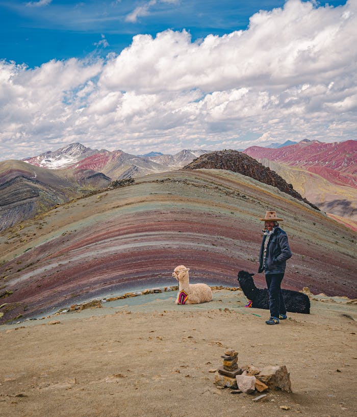 A woman with llamas on the stunning Rainbow Mountain under a bright sky.